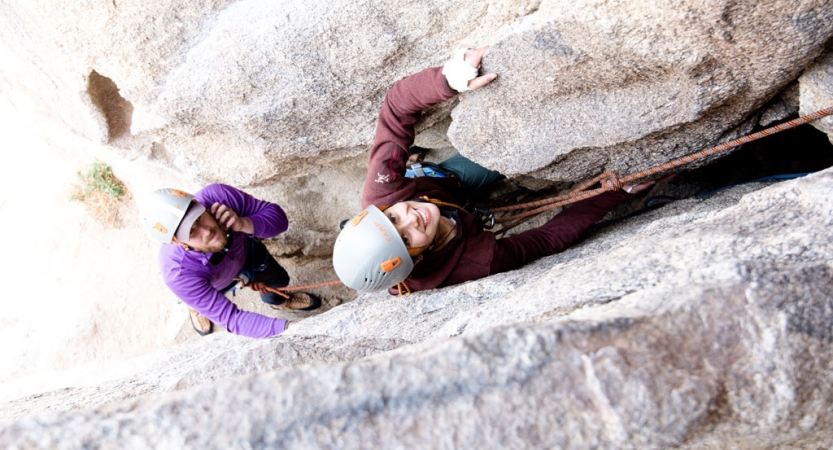 two students in rock climbing gear smile at the camera while navigating a crag 